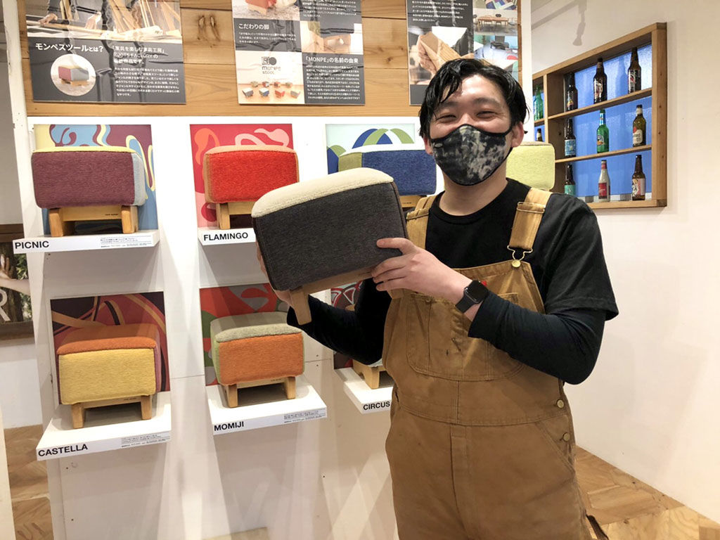 ルーツファクトリーの看板商品の『モンペスツール』を持ち笑顔の福井くん